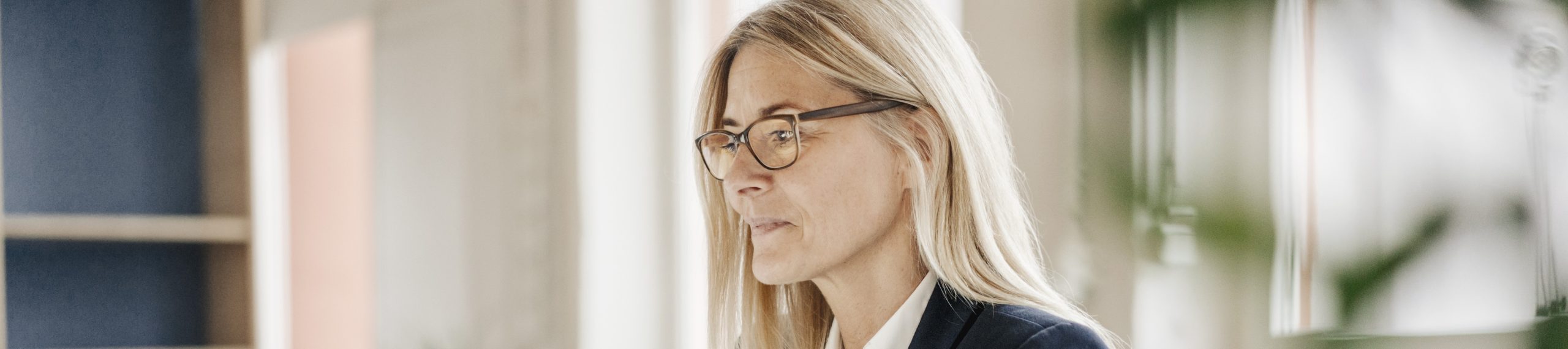 A woman at a desk, looking like she's struggling with her glasses