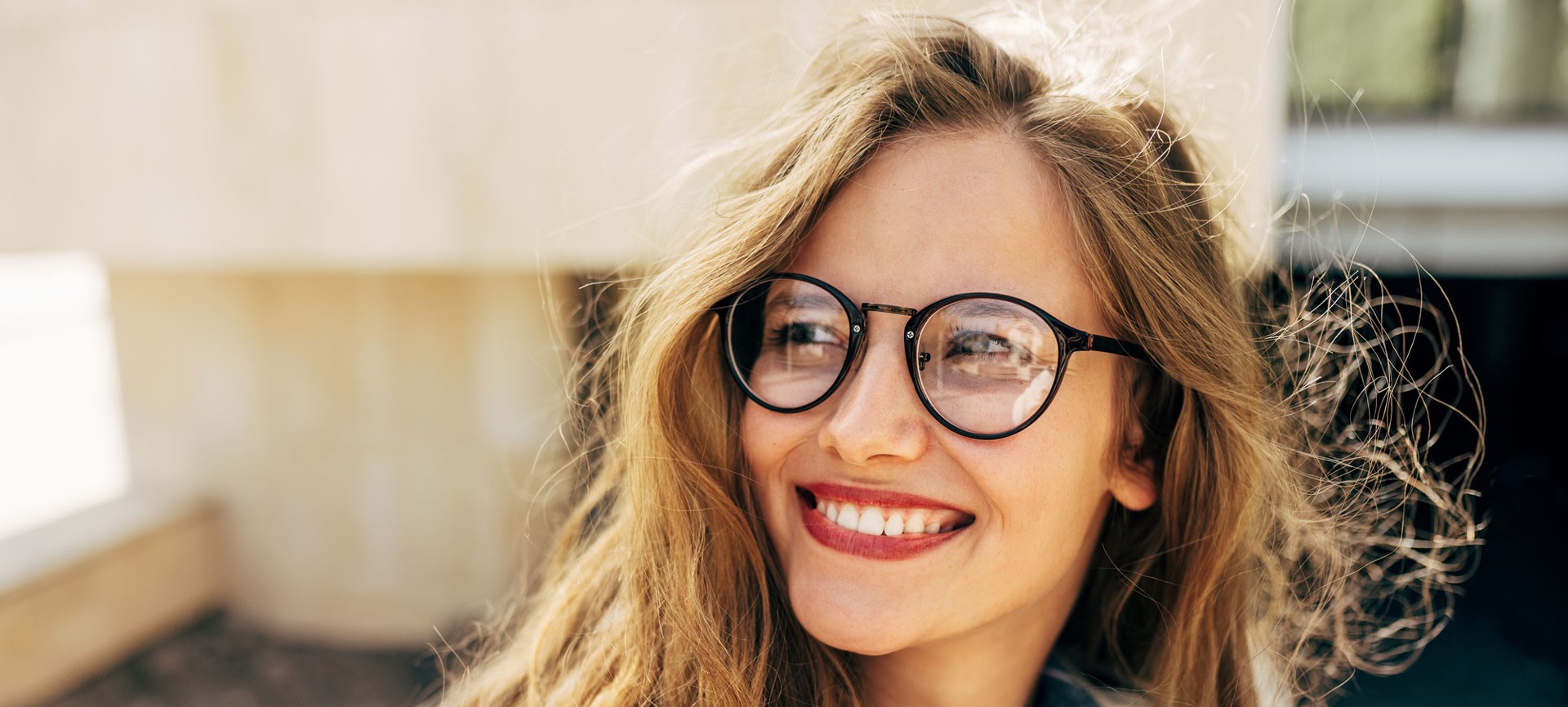new_a-persons-spectacles-reflect-their-character Closeup portrait of a smiling young student woman wearing transparent eyeglasses standing next to the college campus and carrying lots of books and folders on a sunny day.